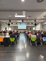 Bild von der Informationsveranstaltung im Aggertal-Gymnasium. Zu sehen sind die Besucher in mehreren Sitzreihen, wie sie einem Vortrag auf dem Podium zuhören.