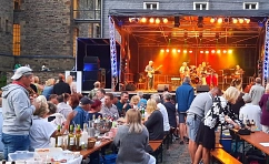 Zu sehen sind die Gäste der Parkzeit. Im Hintergrund ist die Bühne auf der eine Live Band performt. Die Gäste sitzen auf Bierbänken an Biertischen und genießen mitgebrachte Speisen und Getränke.&nbsp;&copy;&nbsp;KulturLeben