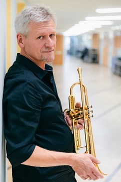 Andy Haderer lehnt sich an eine Wand und hält eine Trompete in den Händen