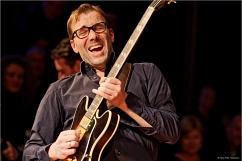 Portrait Bruno Müller Bruno Müller vor einem dunklen Hintergrund während er Gitarre spielt
